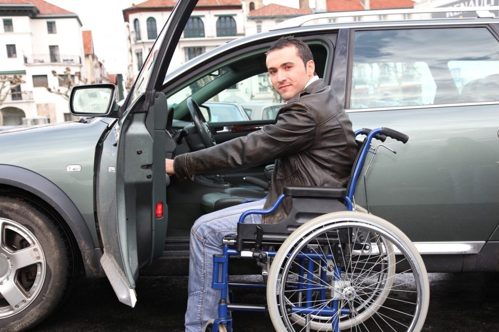 Junger Mann mit Rollstuhl, der gerade ins Auto zu seiner Fahrausbildung einsteigt
