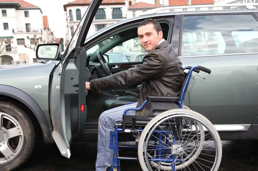 Junger Mann mit Rollstuhl, der gerade ins Auto zu seiner Fahrausbildung einsteigt
